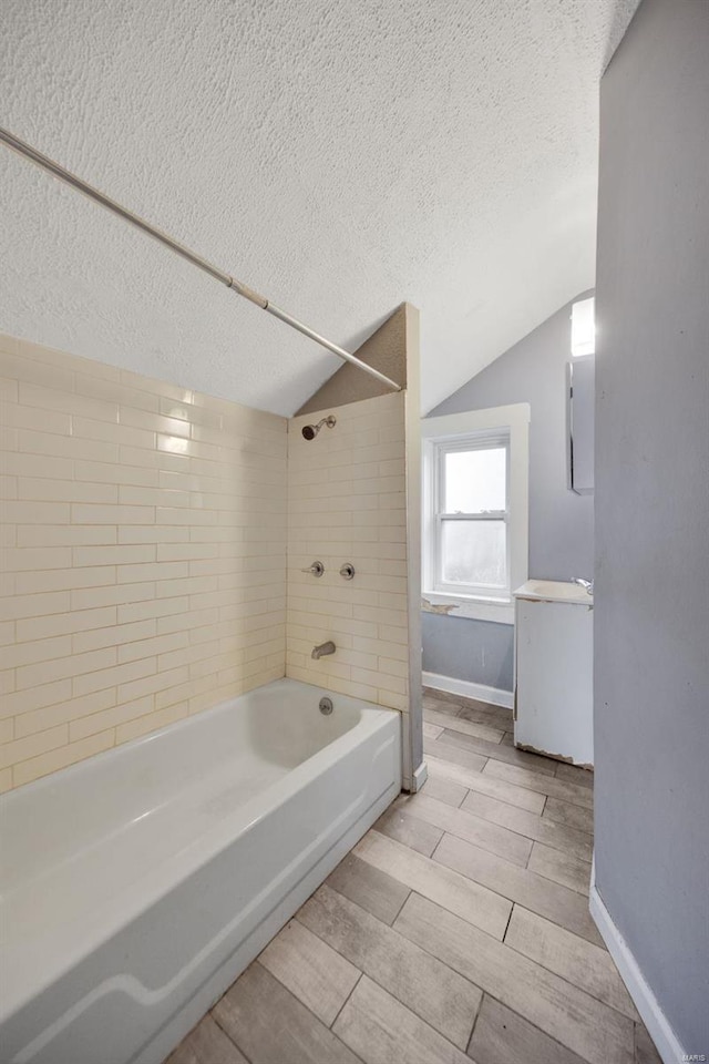 bathroom with tiled shower / bath combo, vaulted ceiling, and a textured ceiling