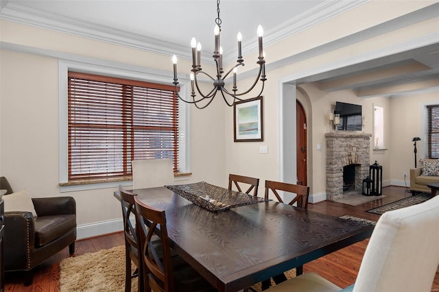 dining space with crown molding, a stone fireplace, dark hardwood / wood-style floors, and an inviting chandelier