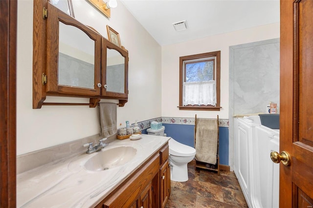 bathroom featuring vanity, toilet, washer and clothes dryer, and a washtub