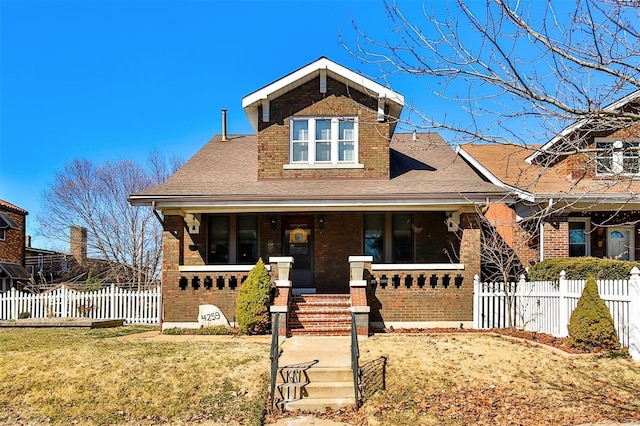 view of front of house featuring covered porch, a front yard, fence, and brick siding