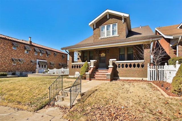 view of front of house featuring brick siding, covered porch, fence, and a front yard