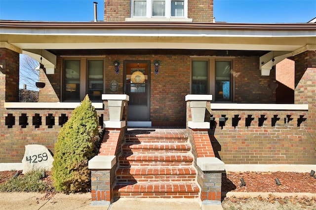 doorway to property with covered porch and brick siding