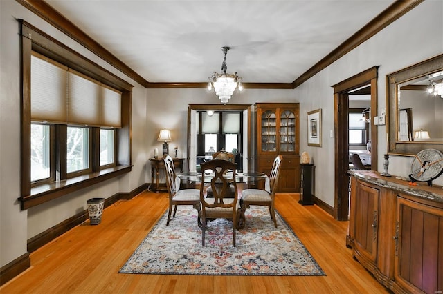 dining space with a chandelier, ornamental molding, light wood-style flooring, and baseboards