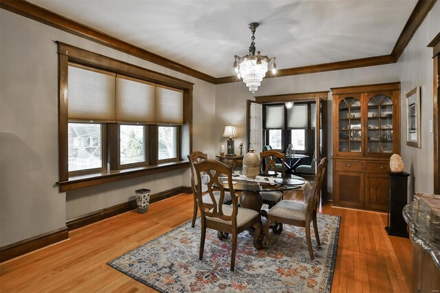 dining space with ornamental molding, light wood-type flooring, baseboards, and an inviting chandelier