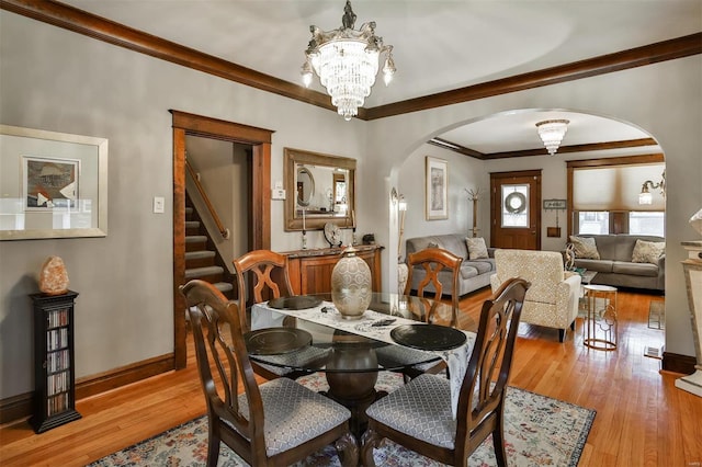 dining room featuring arched walkways, light wood-style flooring, a notable chandelier, baseboards, and ornamental molding