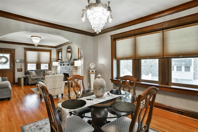 dining room featuring arched walkways, light wood-style flooring, ornamental molding, an inviting chandelier, and a fireplace