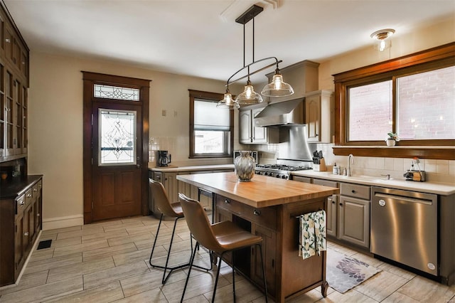 kitchen featuring a sink, wooden counters, stainless steel dishwasher, wall chimney range hood, and decorative backsplash