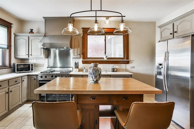 kitchen with a center island, decorative backsplash, appliances with stainless steel finishes, wall chimney range hood, and butcher block countertops