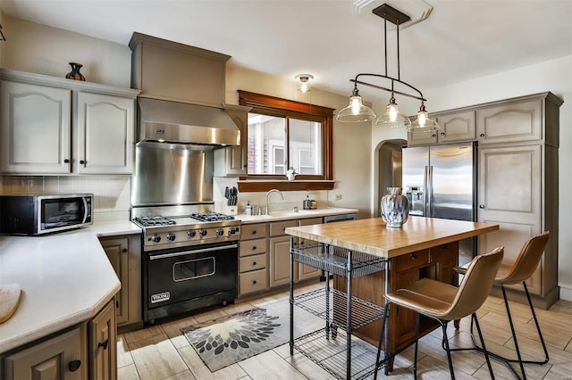 kitchen featuring arched walkways, decorative backsplash, appliances with stainless steel finishes, a sink, and wall chimney range hood