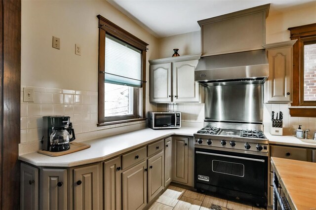 kitchen featuring wall chimney exhaust hood, appliances with stainless steel finishes, wooden counters, and decorative backsplash