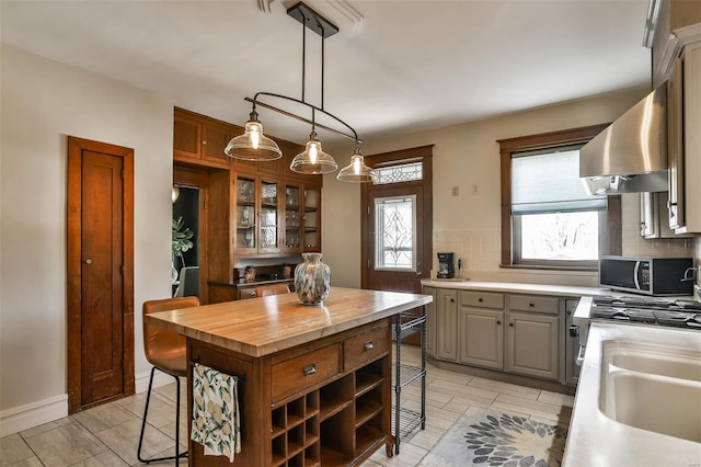 kitchen with butcher block countertops, range hood, stainless steel microwave, and a breakfast bar area