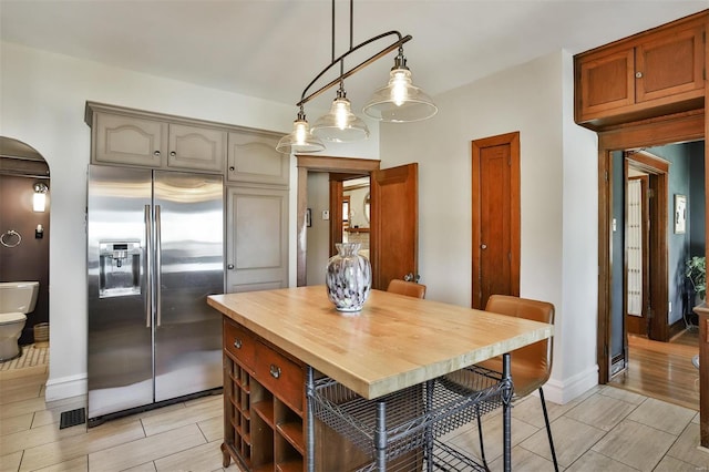 kitchen with wood finish floors, wood counters, stainless steel refrigerator with ice dispenser, a center island, and pendant lighting