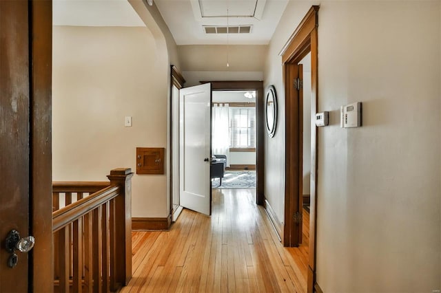 corridor with light wood-style flooring, visible vents, an upstairs landing, baseboards, and attic access