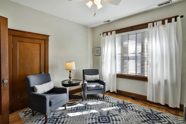 sitting room with a ceiling fan, visible vents, baseboards, and wood finished floors