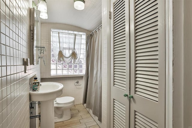 full bath with a shower with shower curtain, toilet, lofted ceiling, wood finished floors, and tile walls