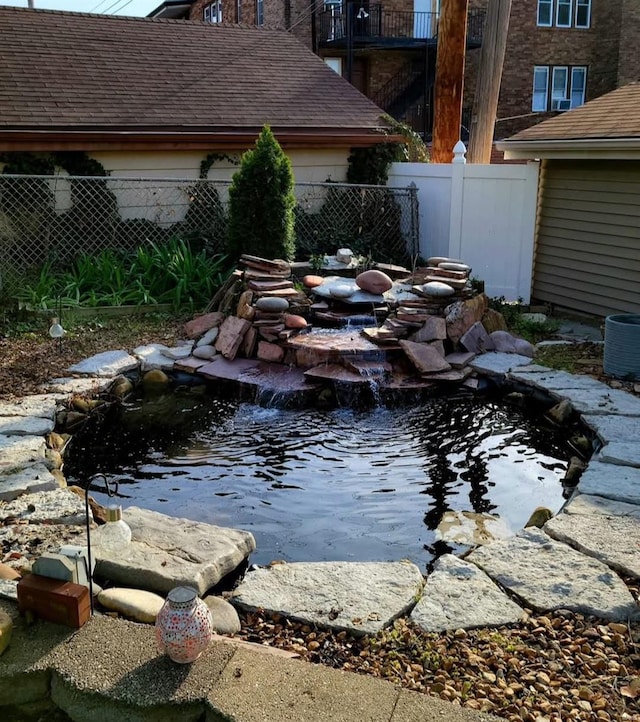 view of yard with fence, a small pond, and central AC unit