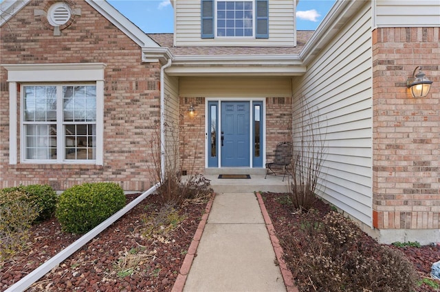 property entrance featuring a shingled roof and brick siding