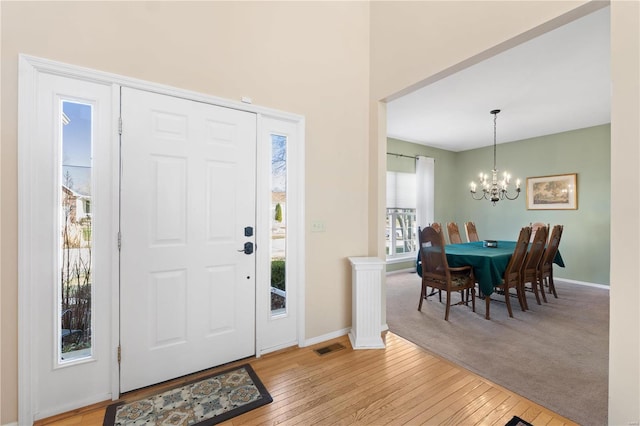 entryway featuring baseboards, light wood-style floors, visible vents, and an inviting chandelier