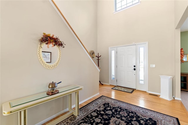 entryway featuring a towering ceiling, baseboards, and wood finished floors