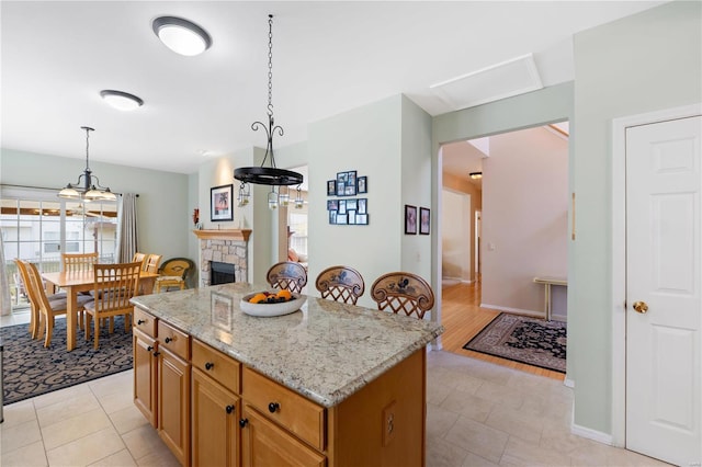 kitchen with baseboards, light stone counters, a center island, decorative light fixtures, and a stone fireplace