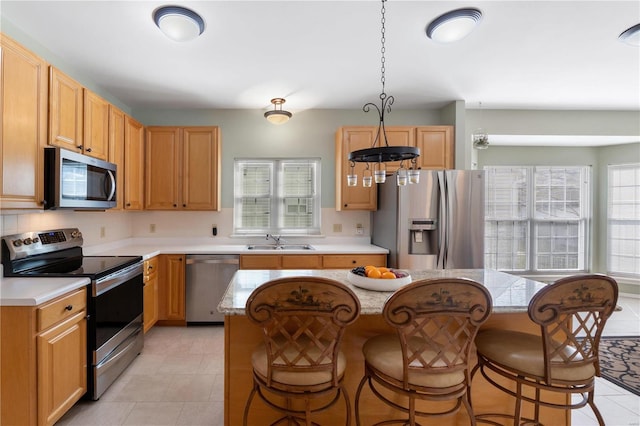 kitchen with a kitchen breakfast bar, hanging light fixtures, stainless steel appliances, light countertops, and a sink