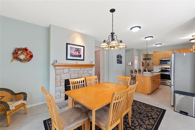 dining space with light tile patterned flooring, a stone fireplace, and baseboards