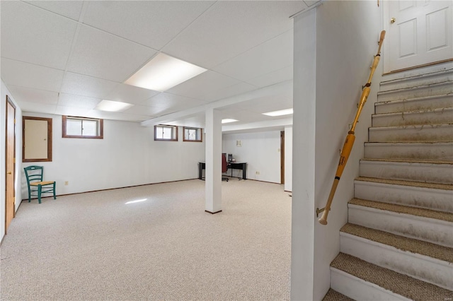 below grade area featuring a paneled ceiling, stairway, and carpet flooring