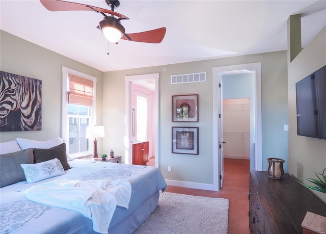 bedroom featuring light carpet, ensuite bath, a walk in closet, and ceiling fan