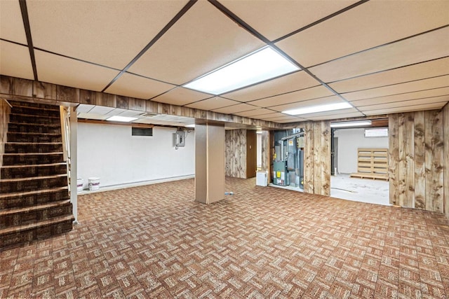 basement featuring a paneled ceiling, electric panel, and wood walls