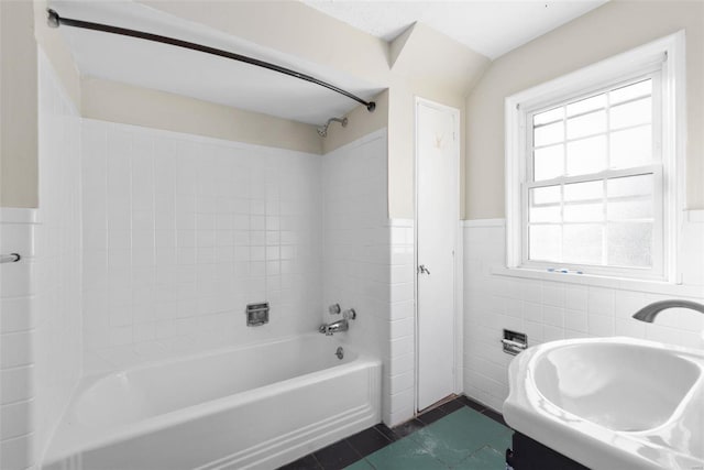 bathroom with tile patterned flooring, sink, tiled shower / bath combo, and tile walls