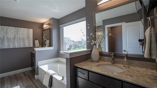 full bath featuring vanity, baseboards, a garden tub, and wood finished floors