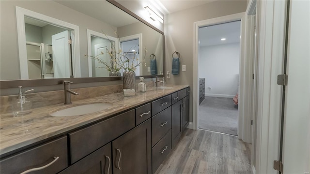 full bath featuring double vanity, a sink, baseboards, and wood finished floors