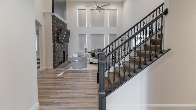 entryway with ceiling fan, a towering ceiling, arched walkways, a fireplace, and wood finished floors
