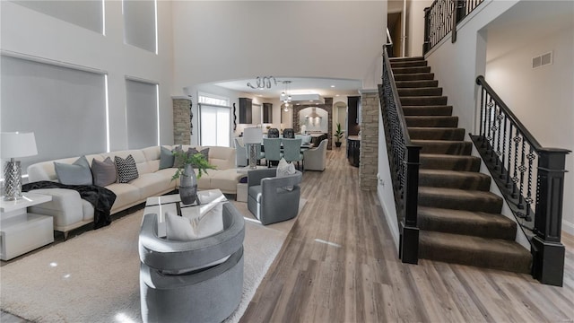 living room featuring visible vents, a towering ceiling, arched walkways, wood finished floors, and stairs