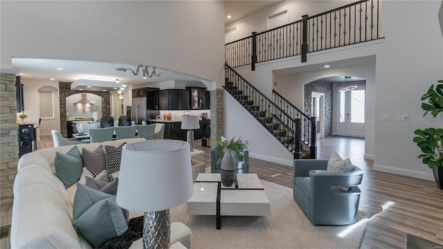living area with arched walkways, baseboards, wood finished floors, a towering ceiling, and stairway