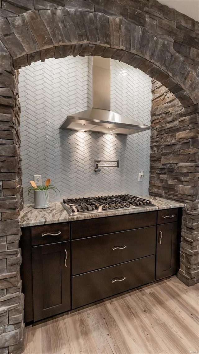 kitchen featuring stainless steel gas stovetop, light wood-style floors, wall chimney exhaust hood, and dark brown cabinetry