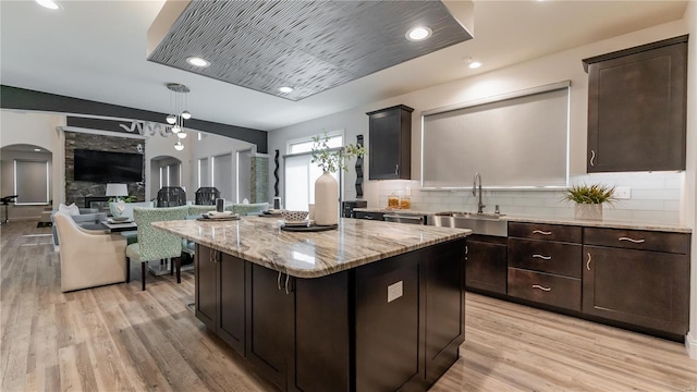 kitchen with dark brown cabinets, light wood-style floors, light stone counters, a sink, and backsplash