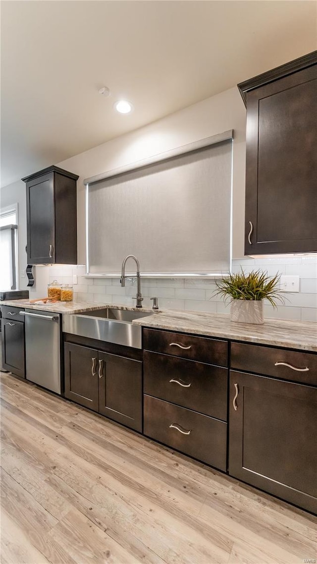 kitchen featuring tasteful backsplash, dark brown cabinets, a sink, dishwasher, and light wood finished floors
