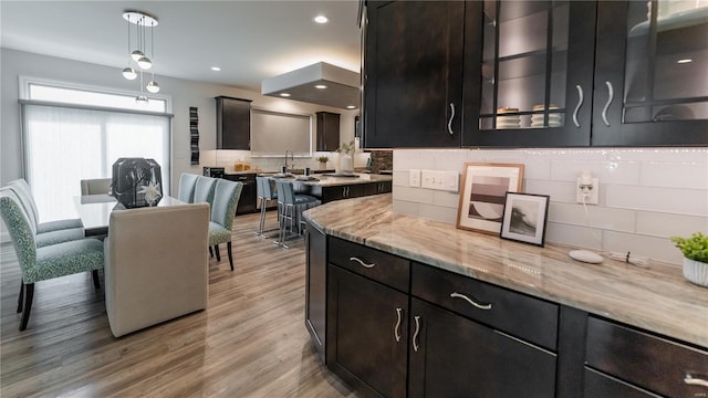 kitchen featuring decorative backsplash, light stone countertops, light wood-style floors, a sink, and hanging light fixtures