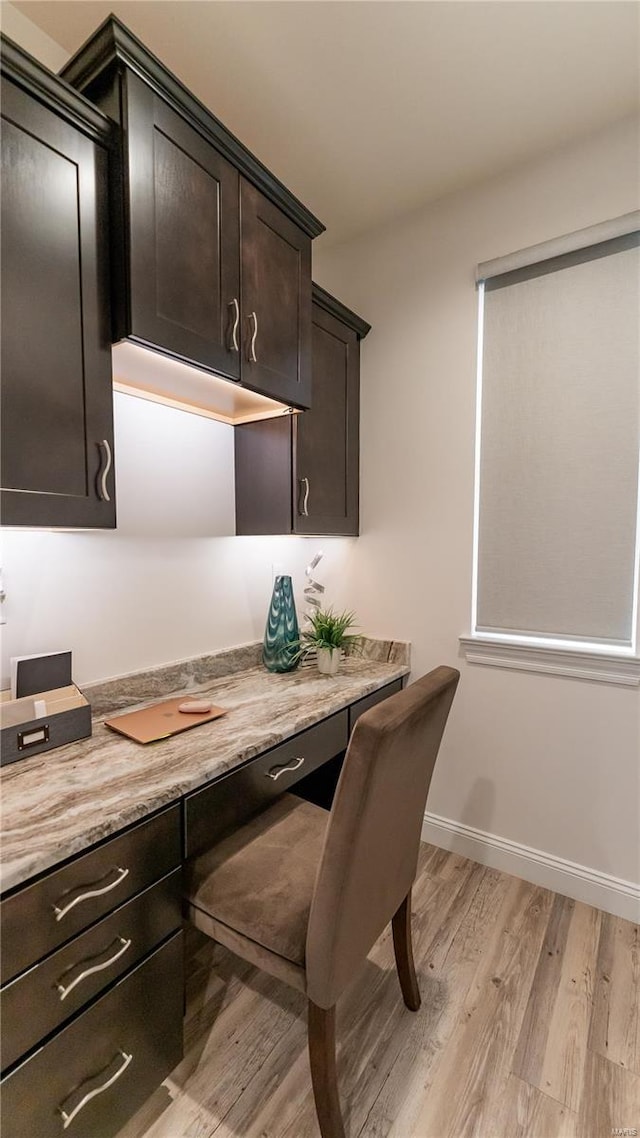 home office featuring built in study area, baseboards, and light wood finished floors