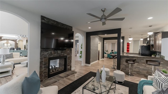 living room with arched walkways, a ceiling fan, and light wood-style flooring