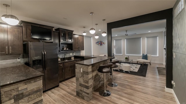 kitchen with dark brown cabinetry, a kitchen bar, fridge with ice dispenser, and light wood-style floors