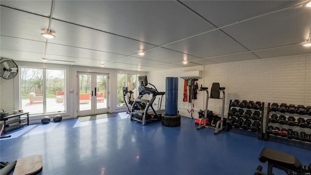 exercise room featuring a wall mounted air conditioner, french doors, and brick wall