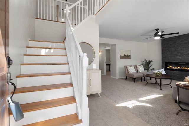 staircase featuring carpet, a fireplace, a ceiling fan, and tile patterned floors