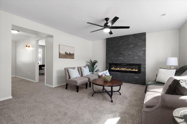 carpeted living room with a ceiling fan, a large fireplace, visible vents, and baseboards