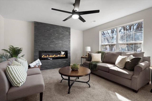 living room featuring carpet, visible vents, ceiling fan, and a stone fireplace