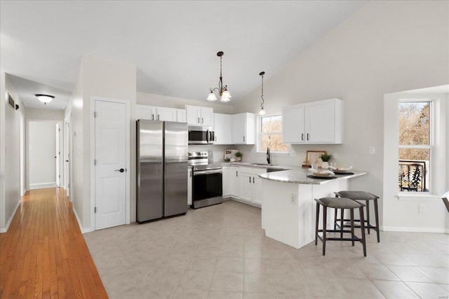 kitchen with stainless steel appliances, white cabinetry, a sink, a peninsula, and a kitchen bar