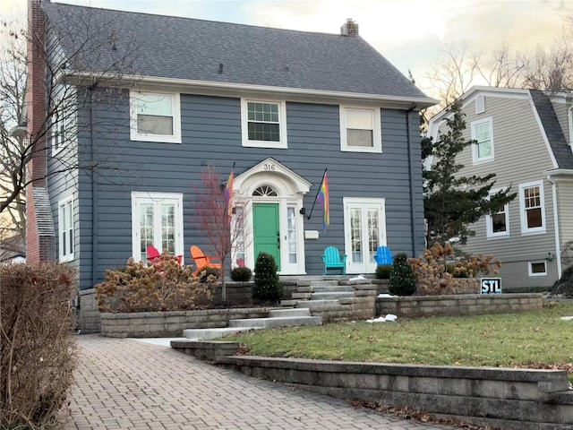 colonial-style house with roof with shingles, a chimney, and a front lawn