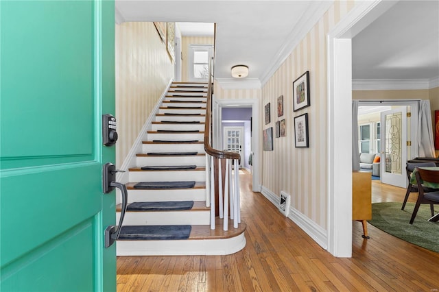 foyer entrance featuring wallpapered walls, baseboards, stairway, wood finished floors, and crown molding