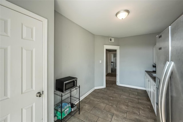 kitchen with stainless steel fridge, dark tile patterned flooring, and white cabinets